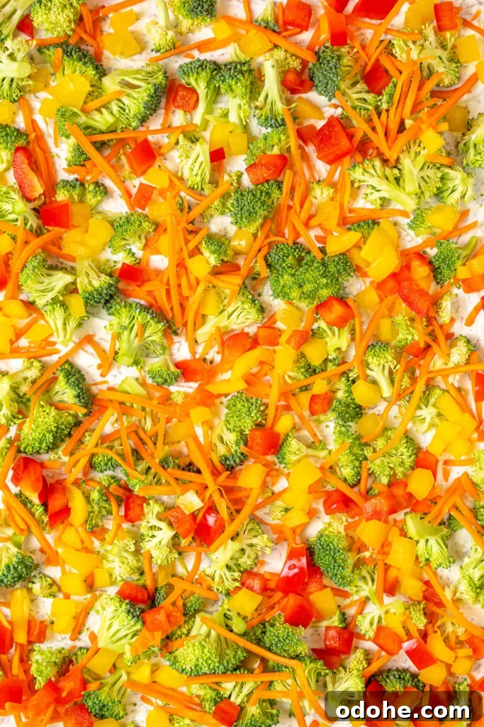 Close up of veggie pizza with dill dip covered in broccoli, carrots, and bell peppers.