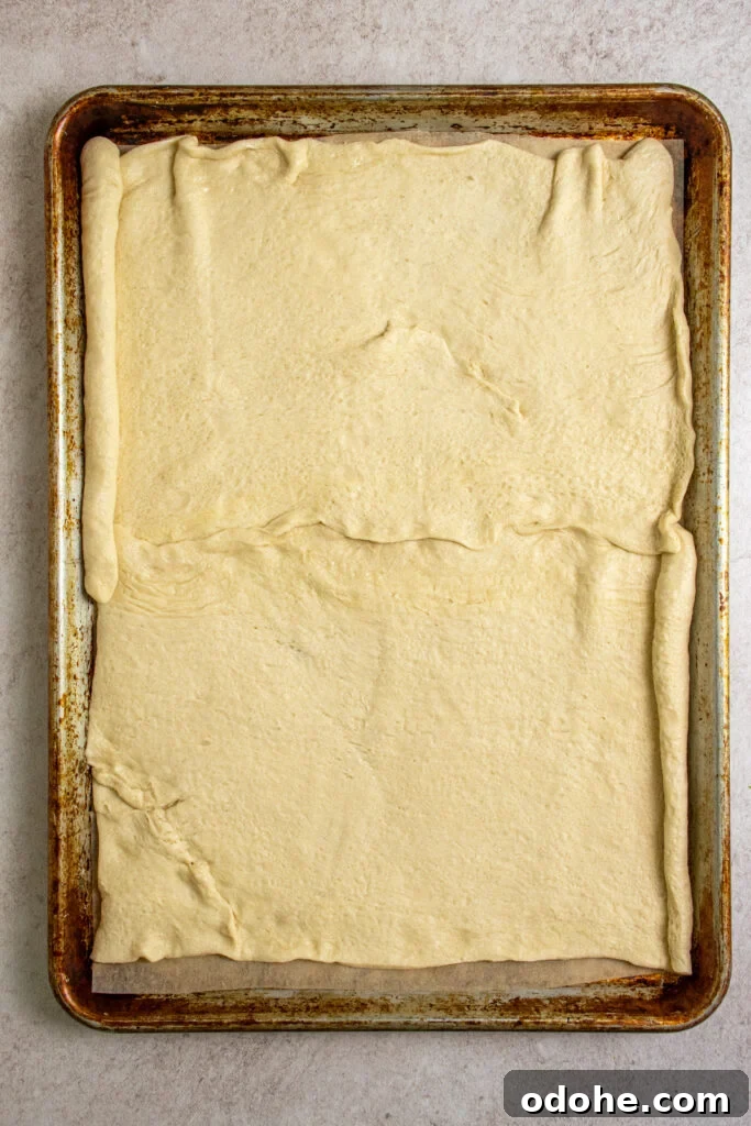 Raw crescent roll dough rolled out on a sheet pan with parchment paper.