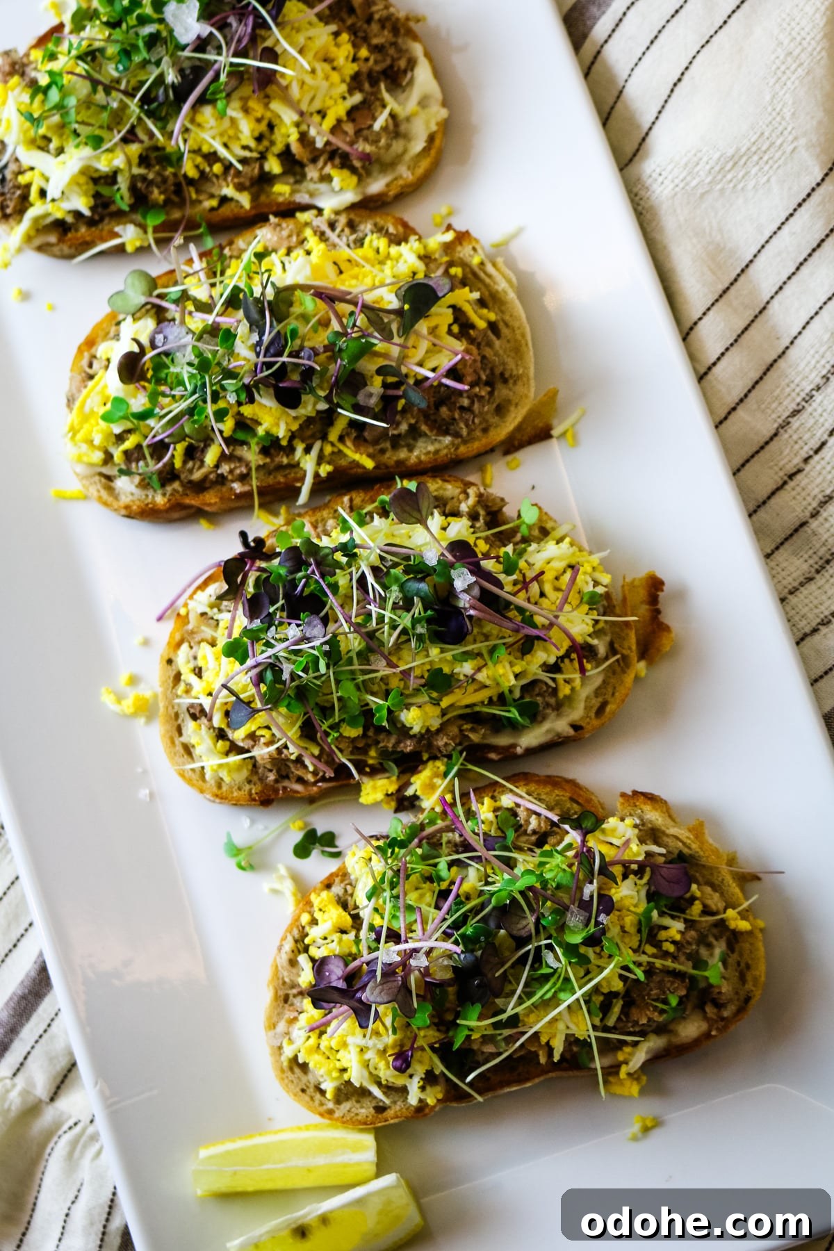 Sardine and Egg Toast Recipe for Brunch or Quick Meals 2 Sardine toast on a white plate, with a lemon on the side.