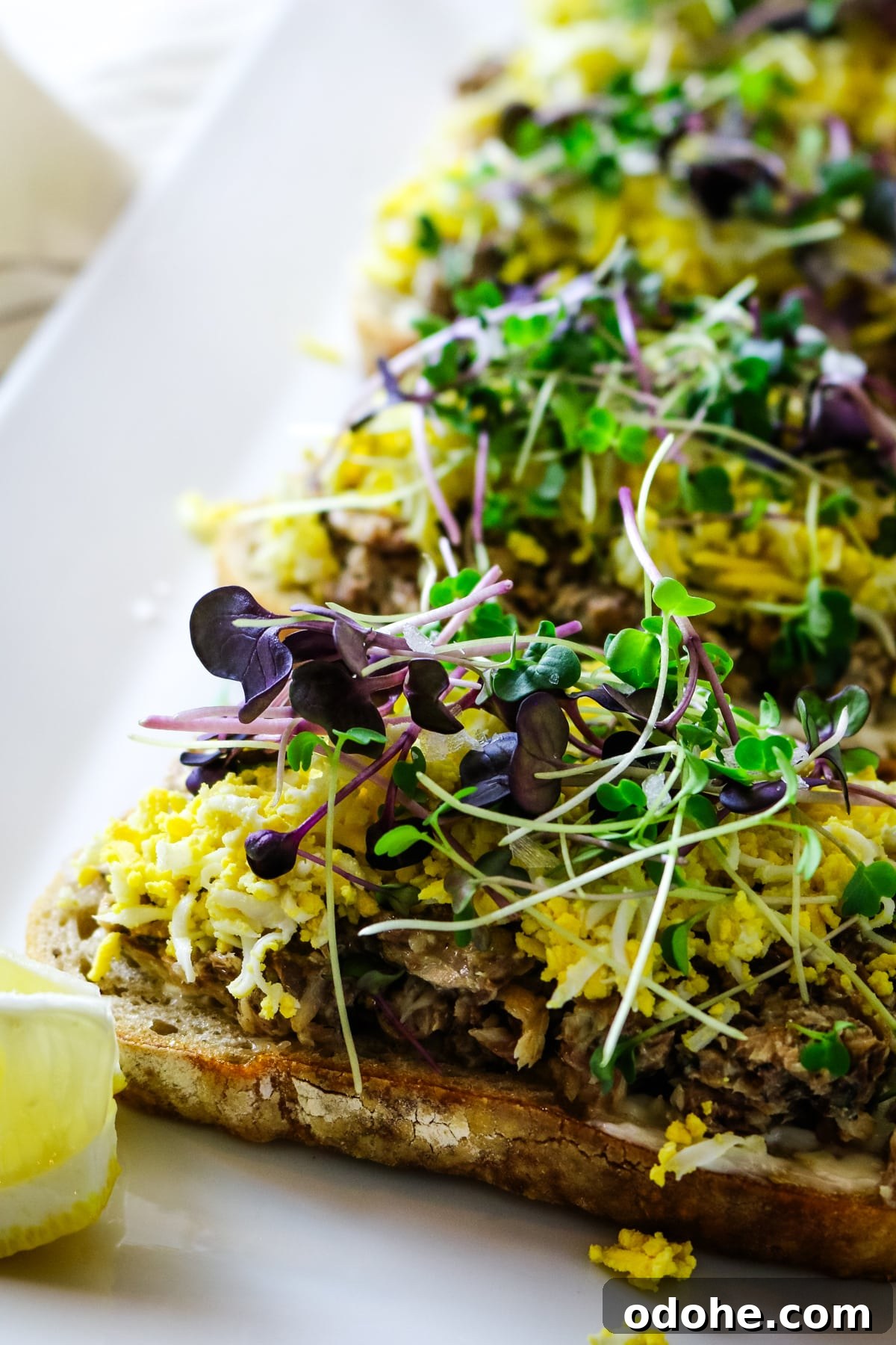 Sardine and Egg Toast Recipe for Brunch or Quick Meals 11 Sardine toast on a white plate, with a lemon on the side.