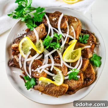 fried beef tongue with sliced white onion and lemon slices.