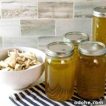 Shredded chicken in a white bowl with five jars of chicken broth beside it.