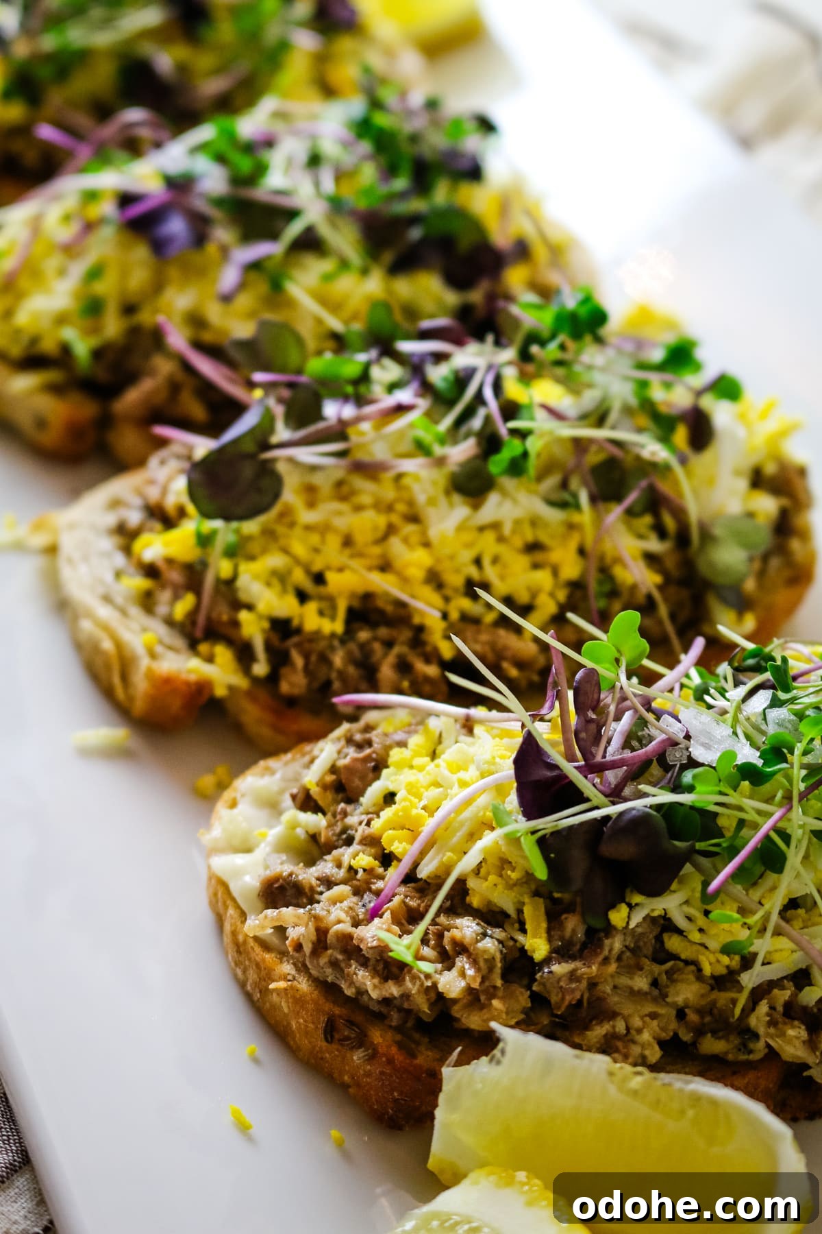 Sardine and Egg Toast Recipe for Brunch or Quick Meals 6 Sardine toast on a white plate, with a lemon on the side.