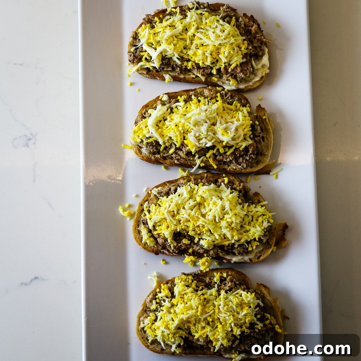 Sardine and Egg Toast Recipe for Brunch or Quick Meals 10 Four pieces of bread with sardines and egg on a white plate.
