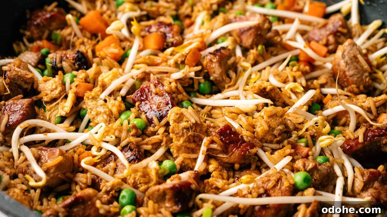 Close-up of fried rice with chunks of meat, peas, diced carrots, and bean sprouts mixed together.
