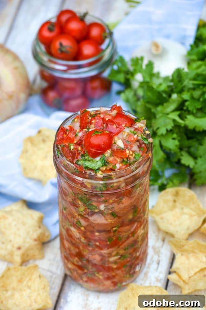 fresh cherry tomato salsa in a glass mason jar surrounded by tortilla chips