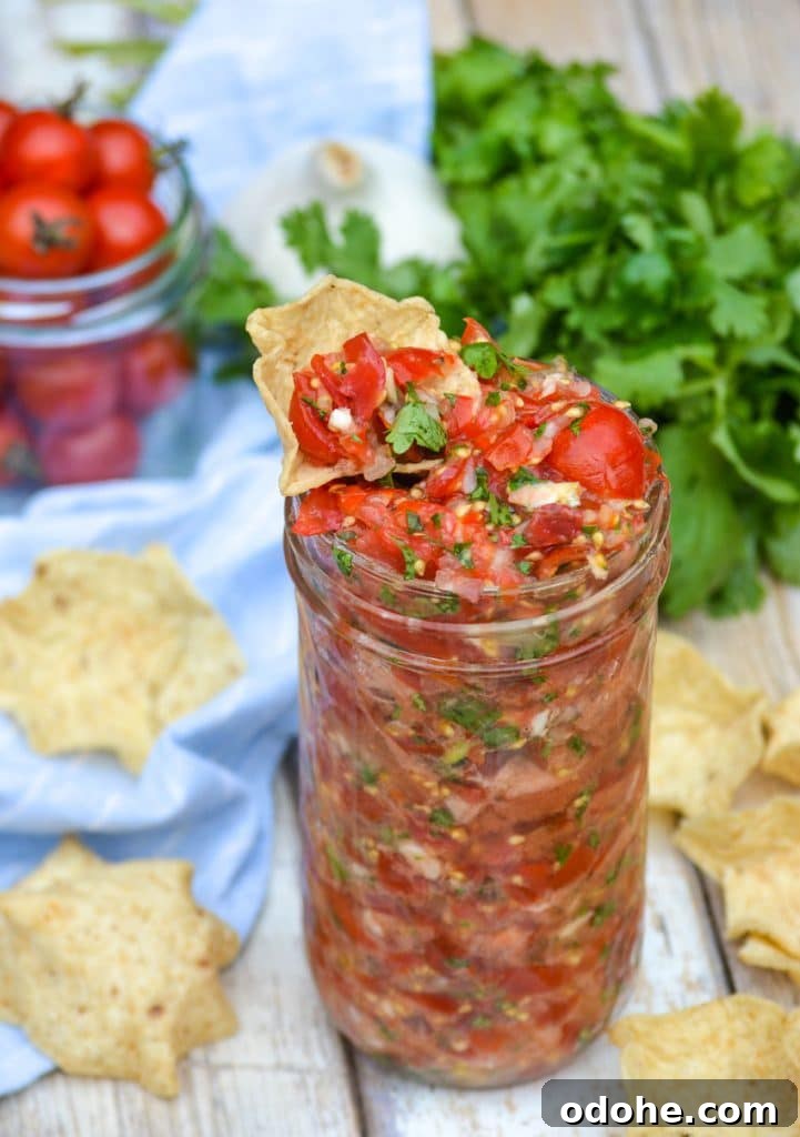 a tortilla chip dipped in a glass jar of sweet cherry tomato salsa