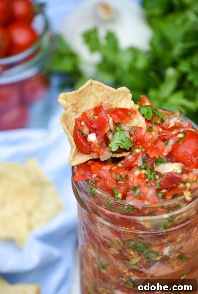 a tortilla chip dipped in a glass jar of sweet cherry tomato salsa