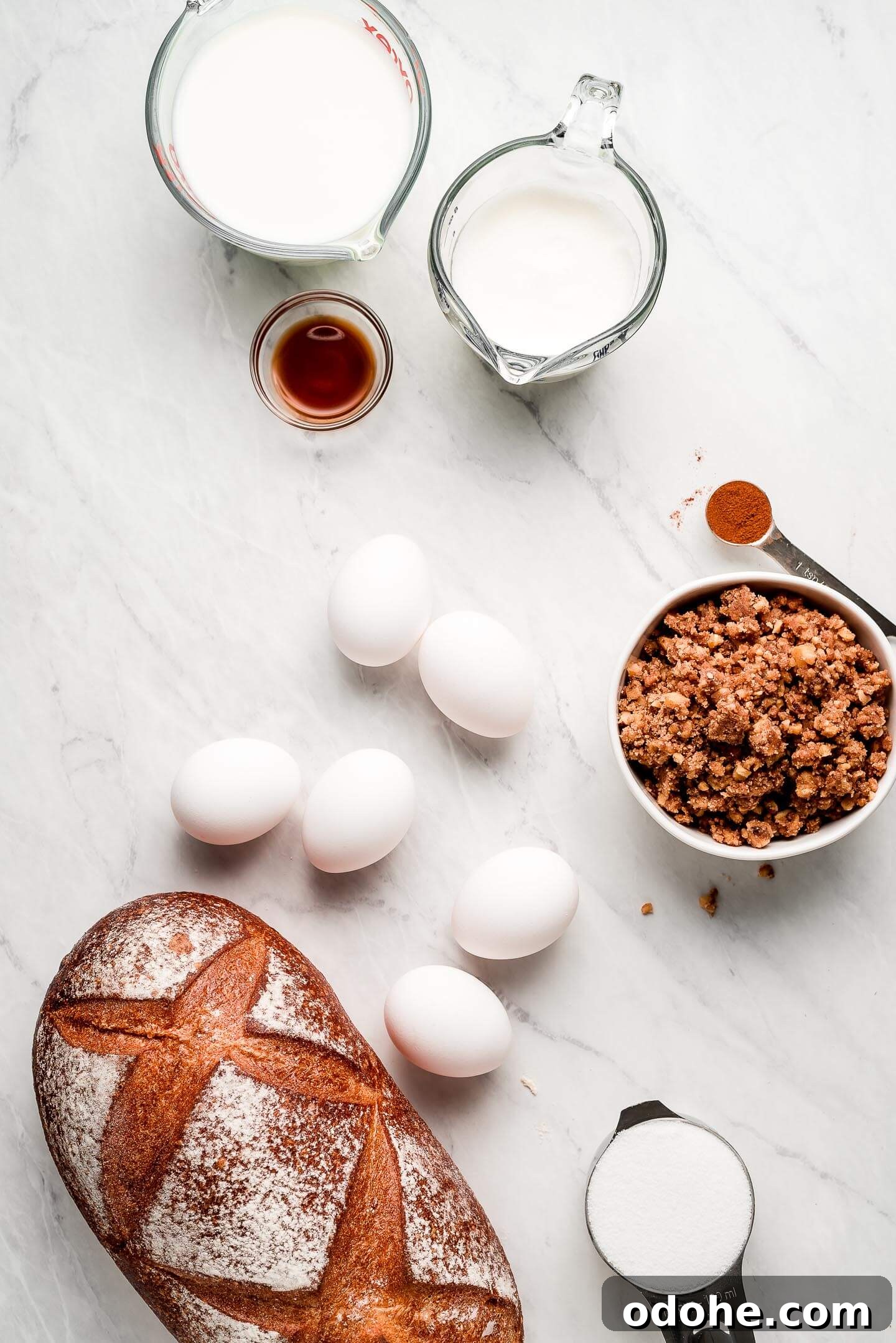 Make-Ahead Overnight French Toast Casserole Recipe 4 Ingredients on a marble surface- milk, cream, vanilla extract, eggs, cinnamon, streusel, sugar, and French bread.