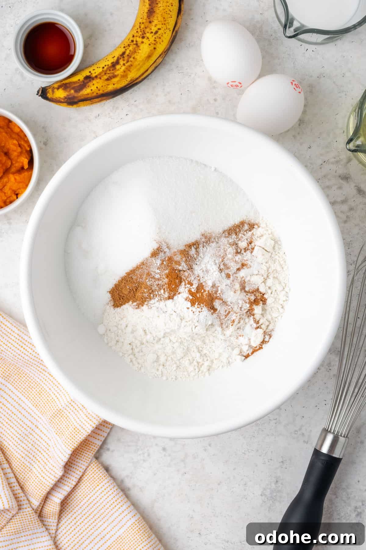 Gluten free flour, sugar, baking powder, baking soda, cinnamon, pumpkin spice and salt combined in a large white mixing bowl.
