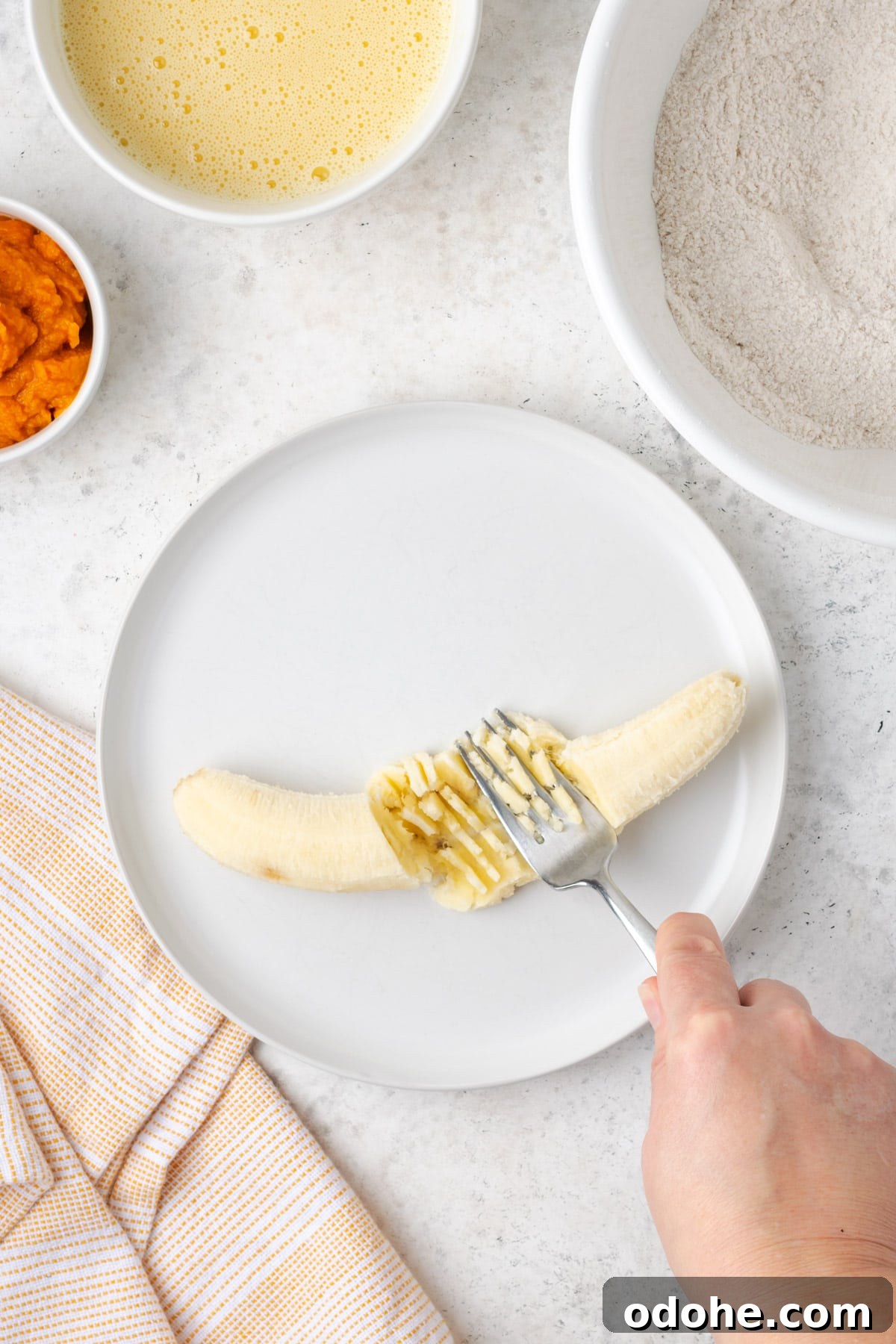 A banana being mashed with a fork on a white plate.