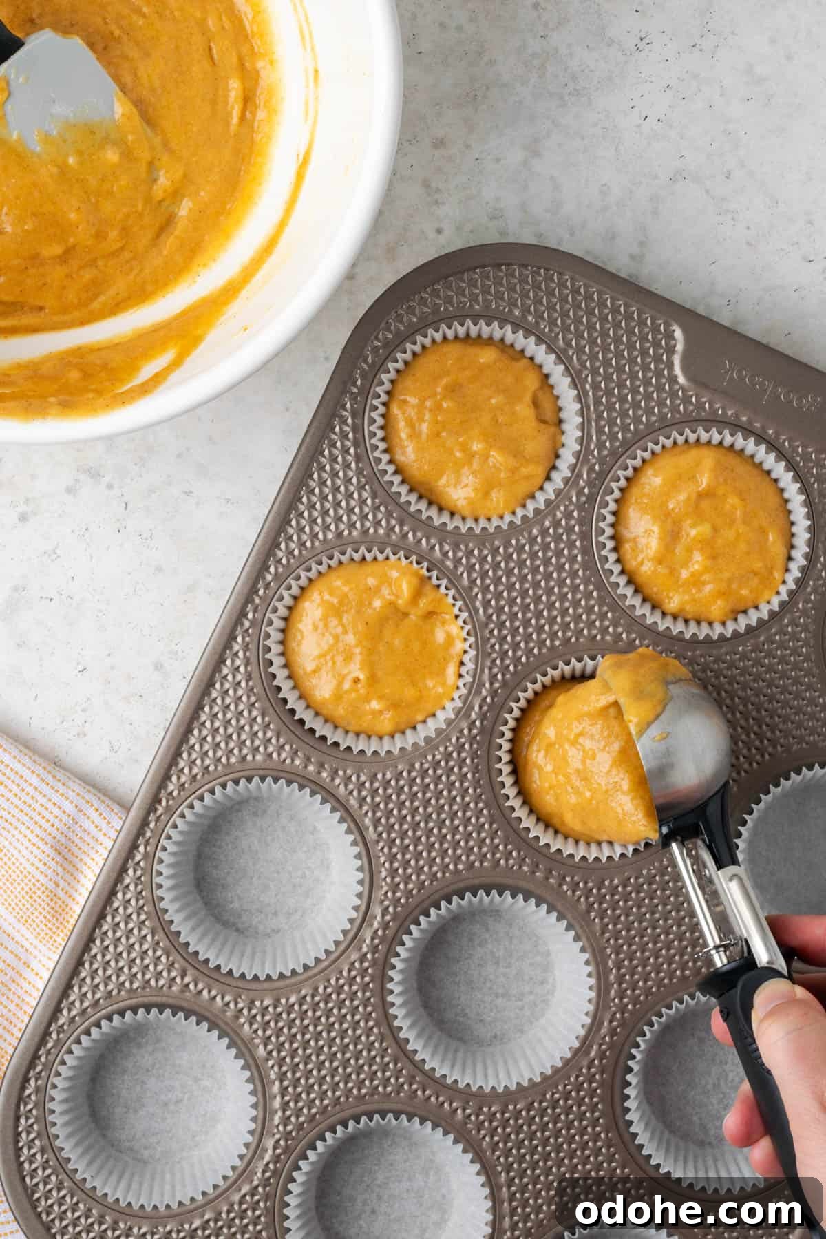 A muffin tin being filled with pumpkin banana muffin batter.