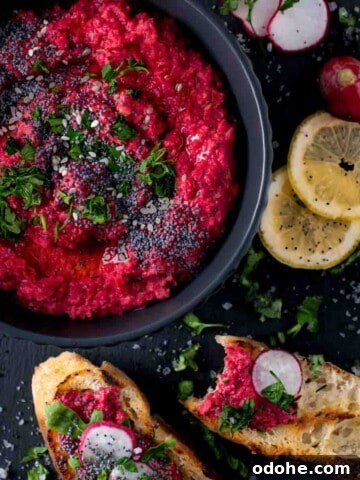 Beetroot hummus in a black bowl with toasted bread and lemon slices on the side.