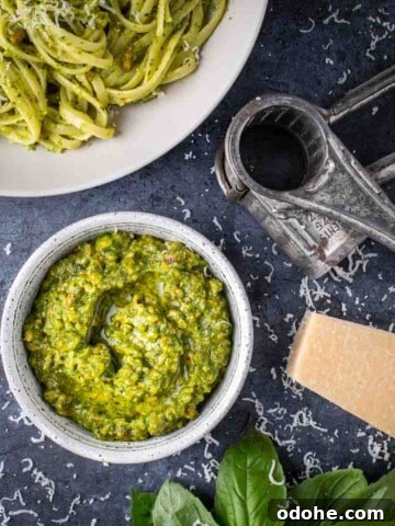 A bowl of pistachio peso surrounded by a bowl of pasta, a parmesan grater and parmesan cheese.