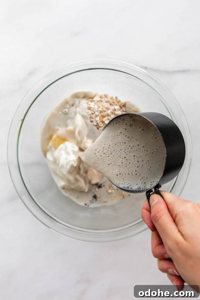 a measuring cup pouring oat milk into a bowl of oats