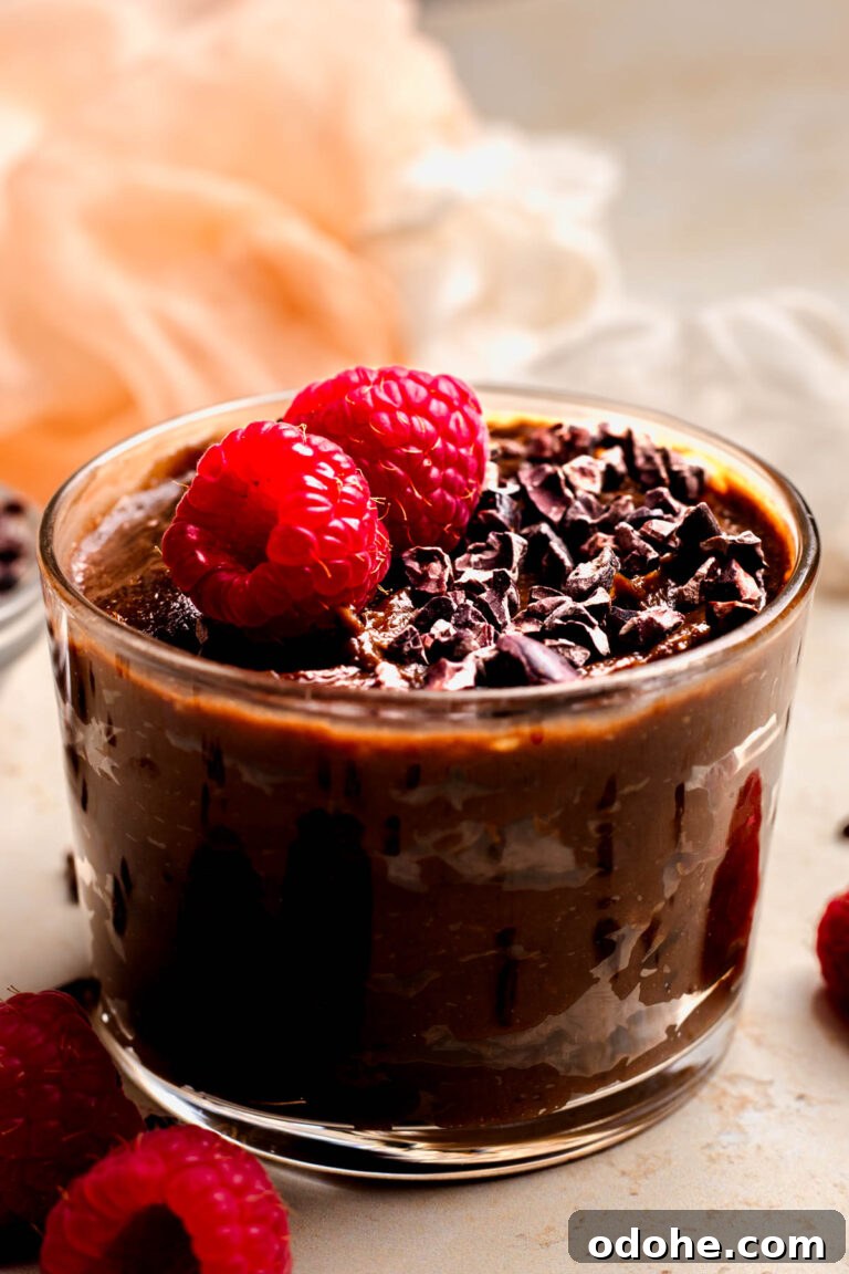 Clear glass bowl of Vegan Chocolate Mousse topped with chocolate shavings and fresh raspberries.