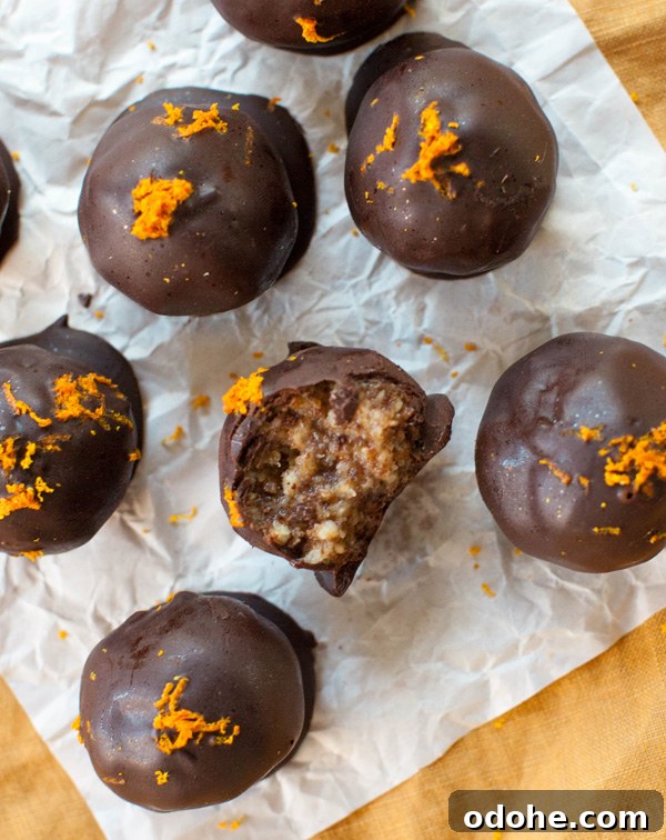 Citrus Chocolate Truffles topped with orange zest on parchment paper. One with a bite taken from it.