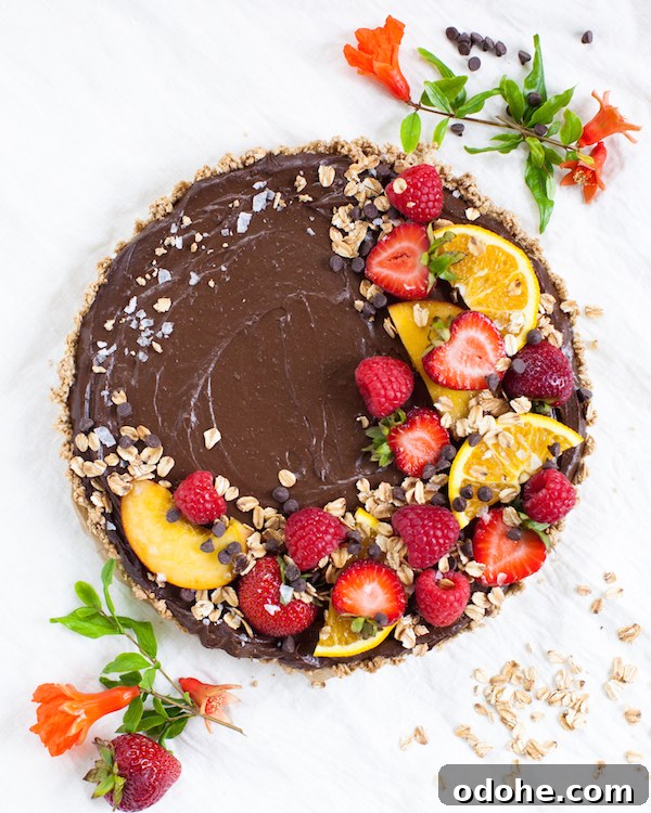 Oatmilk Chocolate Mousse Tart topped with sliced fresh fruit, oats, and flaky sea salt next to fresh flowers.