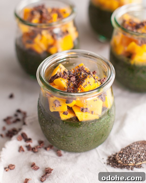 Clear jar of green Spirulina Chia Seed Pudding topped with fresh mango and cacao nibs.
