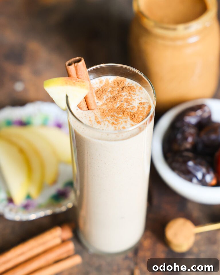 Tall glass of Apple Smoothie with a cinnamon stick and slice of apple on the rim.