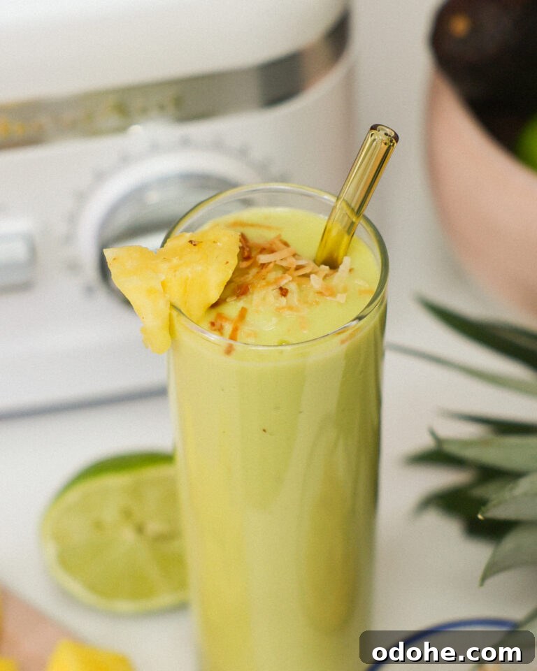 Glass of Energizing Avocado Smoothie with a straw topped with toasted coconut and a slice of fresh pineapple.