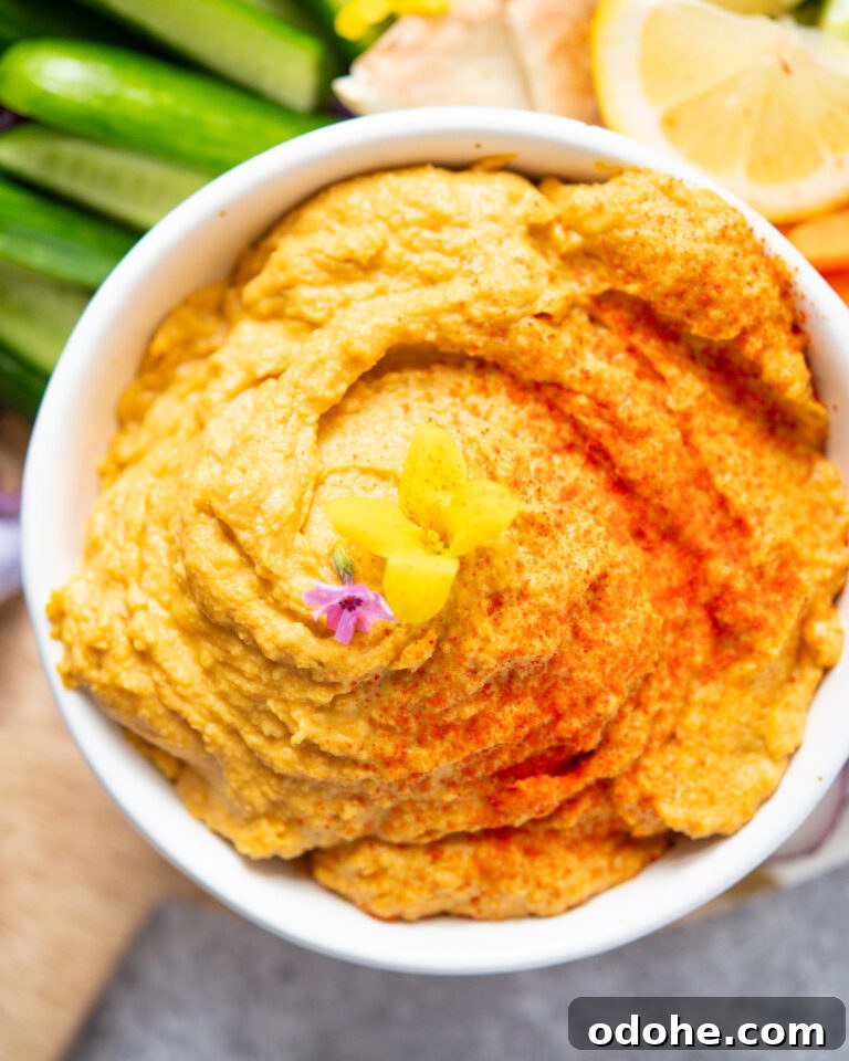 Sweet Potato Hummus in a small bowl, sprinkled with smoked paprika and two edible flowers.