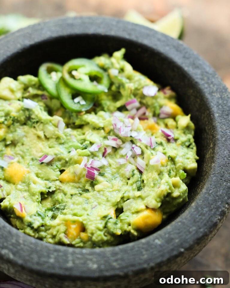 Mango Guacamole in a mortar topped with sliced jalapeño and diced red onion.