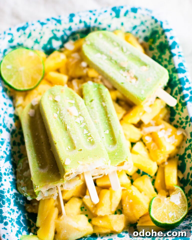 Pan filled with sliced pineapple and lime slices underneath four Avocado Pineapple Popsicles.
