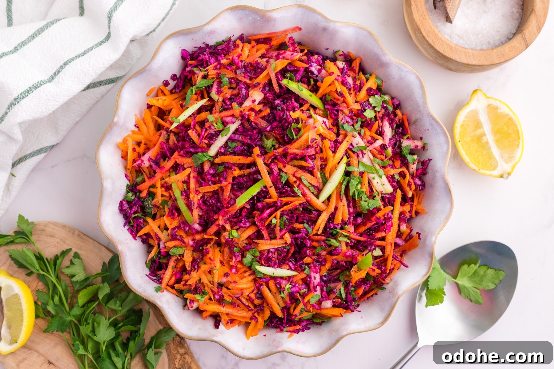 Crunchy Cabbage and Carrot Salad with Zesty Dressing 8 A bowl of cabbage and carrot salad on a white countertop, with lemon and parsley on the table.