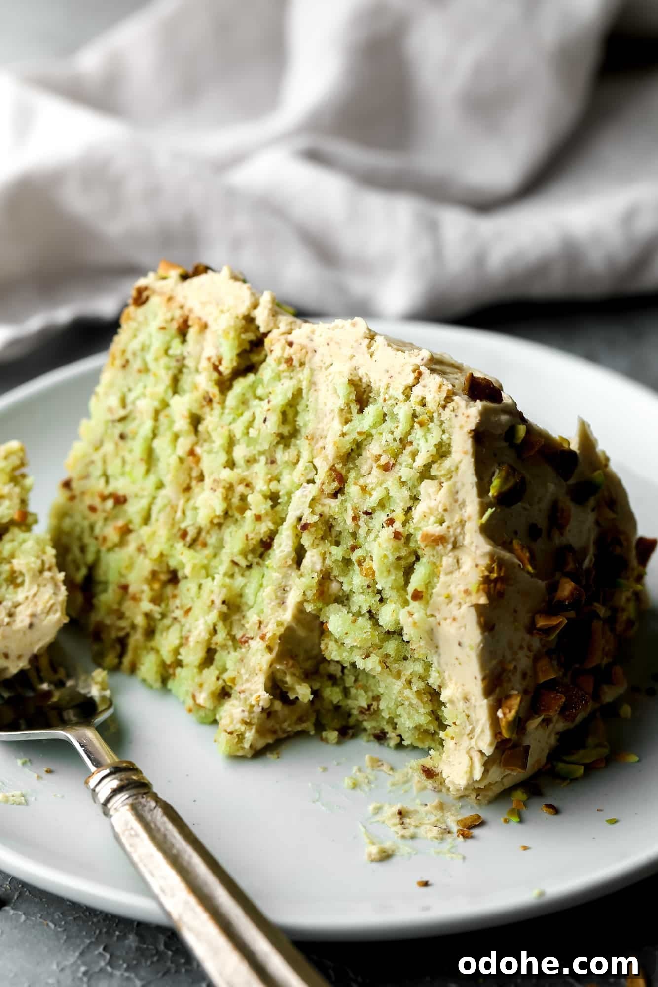 close up on a slice of vegan pistachio cake on a white plate with a bite missing.