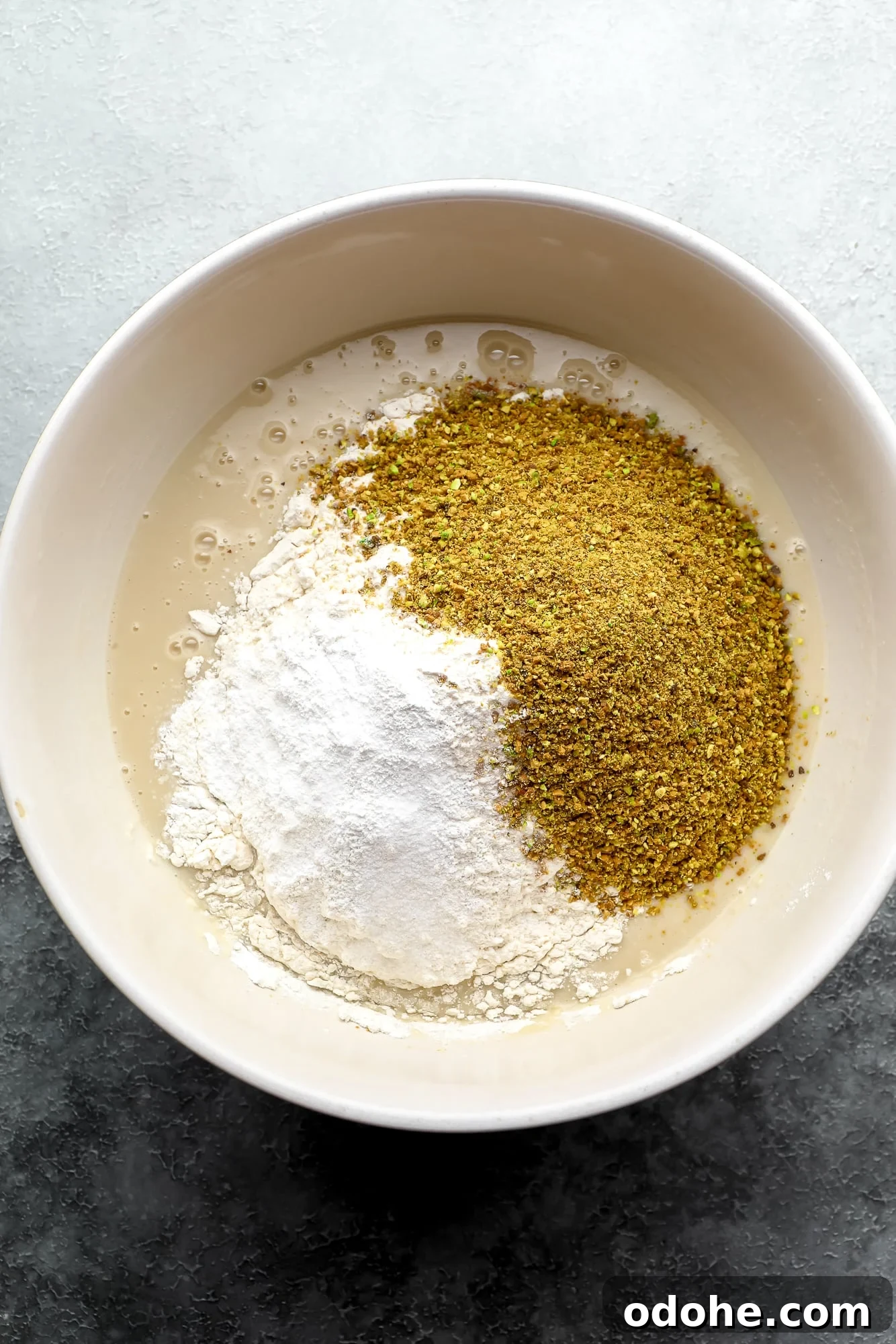 wet and dry ingredients for vegan pistachio cake in a large white bowl.