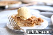 small white plate with a slice of dutch apple pie on it and a fork. there is also a scoop of ice cream on top of the pie