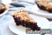a slice of blueberry pie with a crumble topping on a white plate. A second slice is in the background and you can also see a corner of the pie pan the slices came out of.
