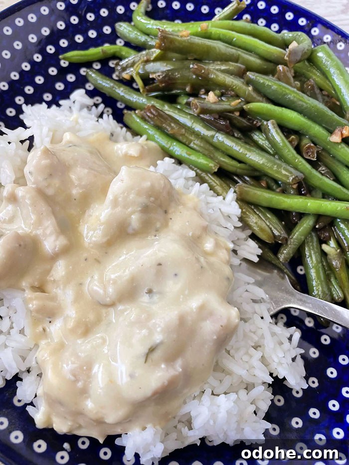 A dark blue Polish pottery dinner plate with white polka dots with a serving of green beans and creamy italian chicken served over white rice with a fork inserted partially under the rice on the plate.
