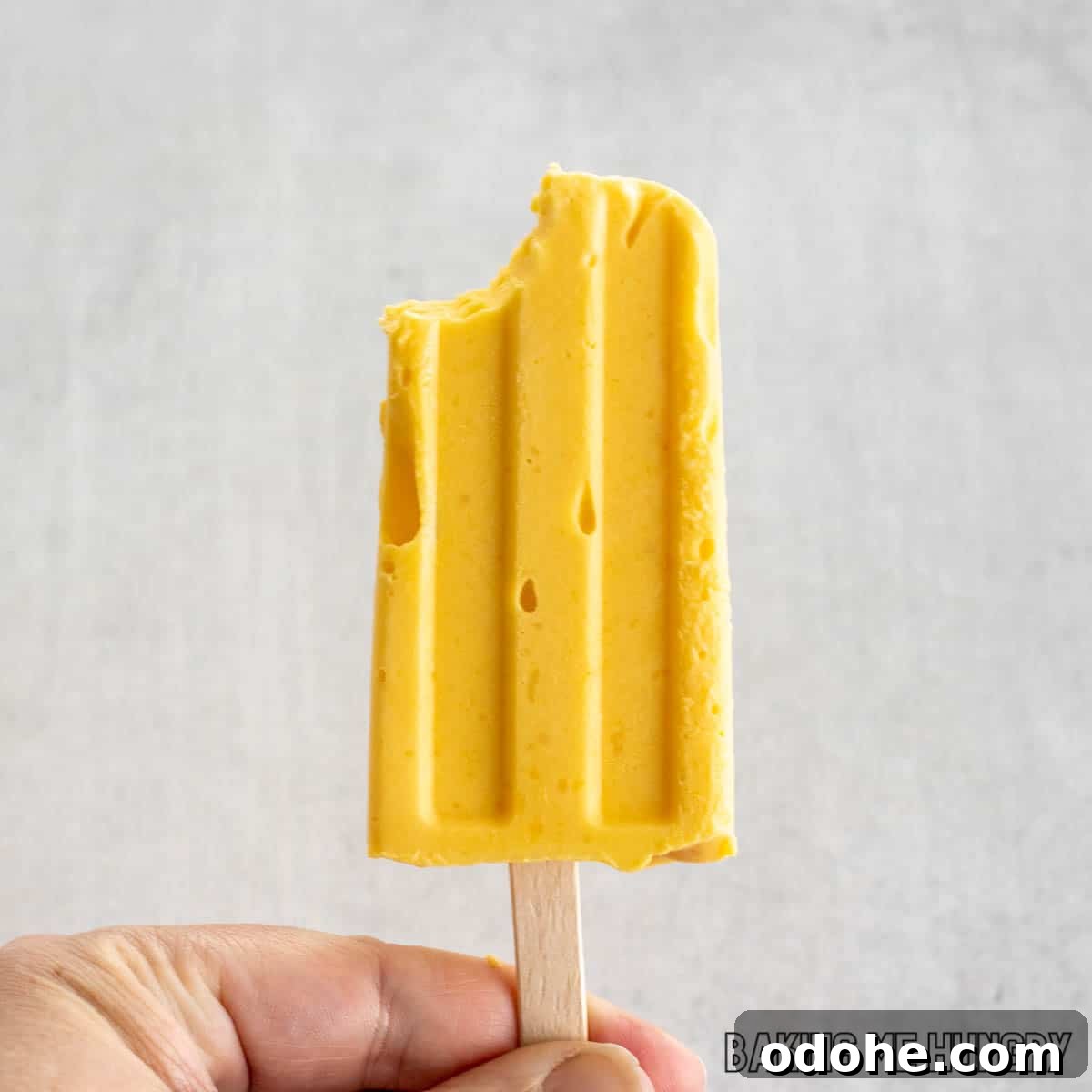 Homemade Mango Popsicle Recipe — Creamy & Refreshing 5 hand holding one of the mango popsicles with a bite missing