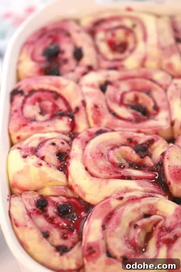 Triple berry sweet cinnamon rolls rising in a baking dish.