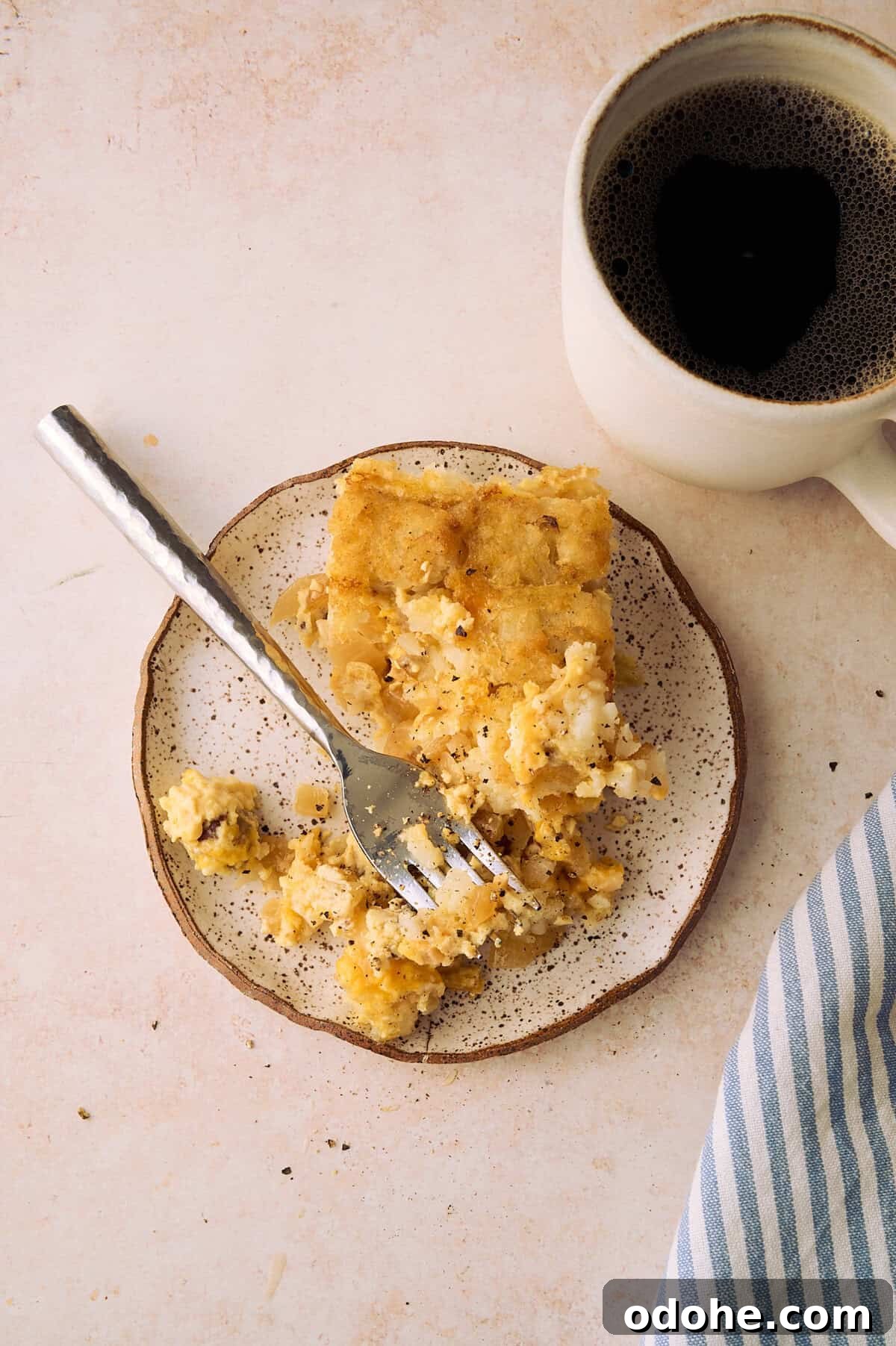 Tater Tot Breakfast Casserole Recipe for Brunch Crowd 11 The tater tot casserole is on a plate with a striped napkin and a cup of coffee next to the plate.