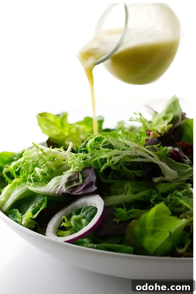 A glass pitcher pours creamy dressing over fresh tossed green salad.