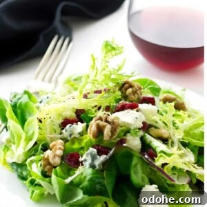 Green salad with walnuts, cranberries, gorgonzola cheese on white plate; wine behind.