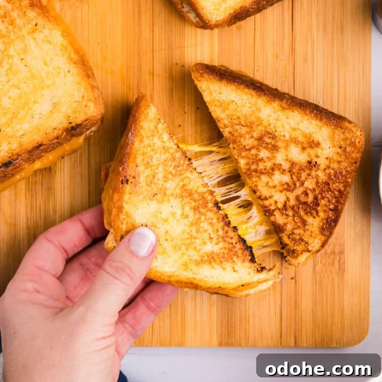 Perfect Grilled Cheese on a Blackstone Griddle: Melted & Crispy 11 Closeup square image of Blackstone Grilled Cheese being pulled apart on wood tray