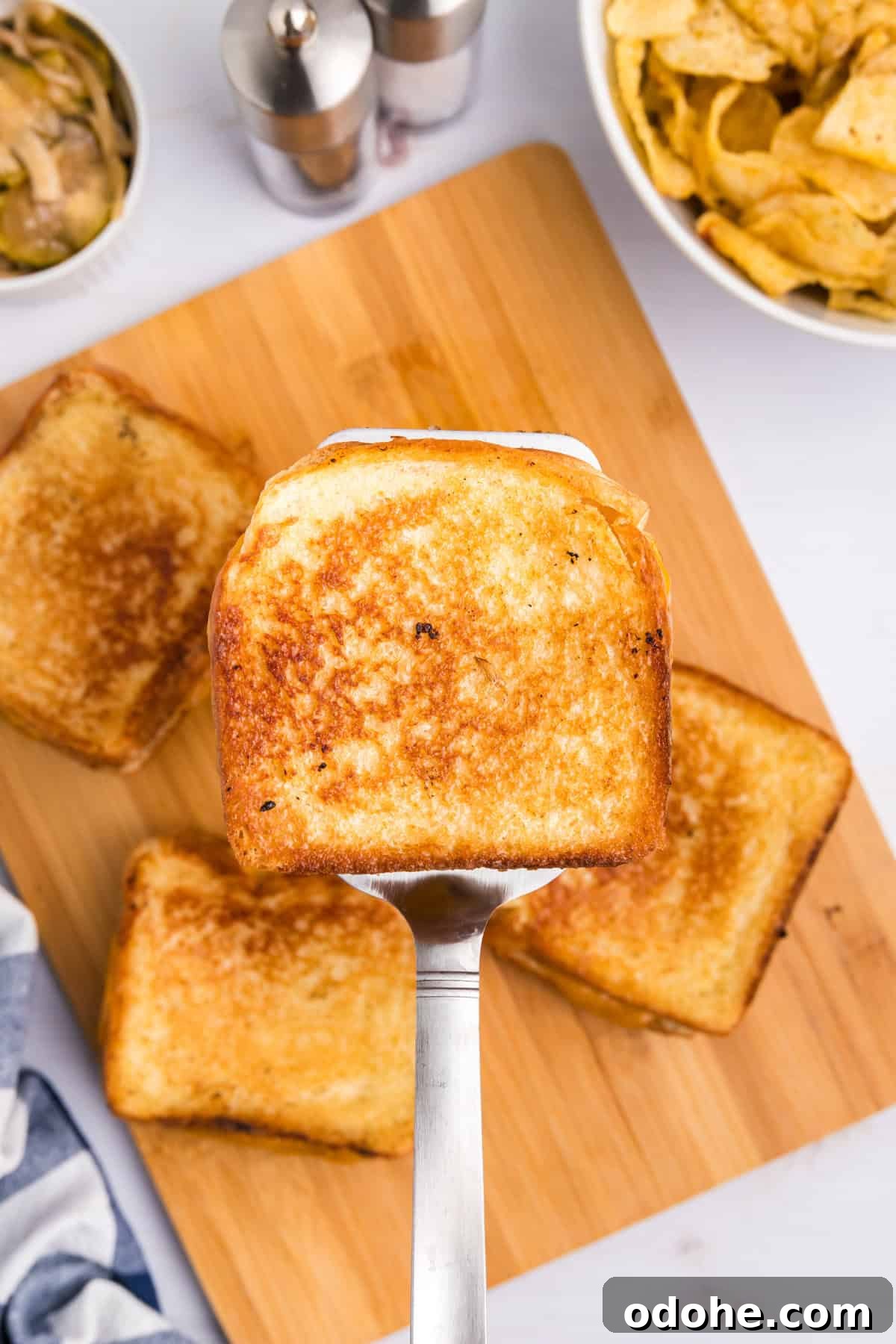 Perfect Grilled Cheese on a Blackstone Griddle: Melted & Crispy 9 Using metal spatula to lift a Blackstone Grilled Cheese from stack on wood serving tray