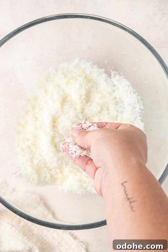 A hand rubbing the lemon zest with the white sugar.