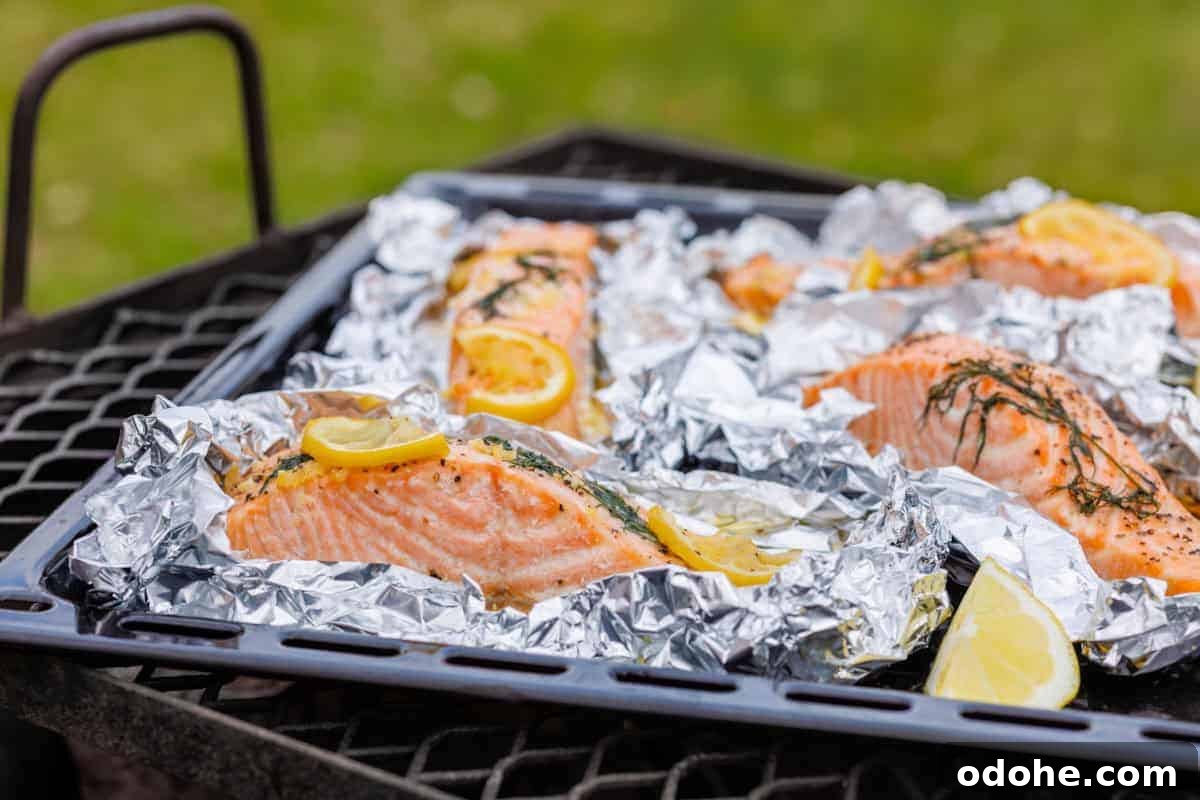 31 Memorial Day Recipes to Start Cookout Season Right 2 Four servings of lemon-dill salmon in foil packets, with lemon slices and dill on top, arranged on a black grill grate with a green grass background.