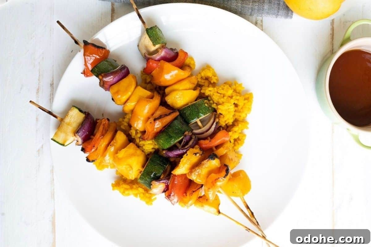 31 Memorial Day Recipes to Start Cookout Season Right 11 Three Grilled Teriyaki Mango Skewers with bell peppers, zucchini, and onions served on a bed of yellow rice on a white plate.