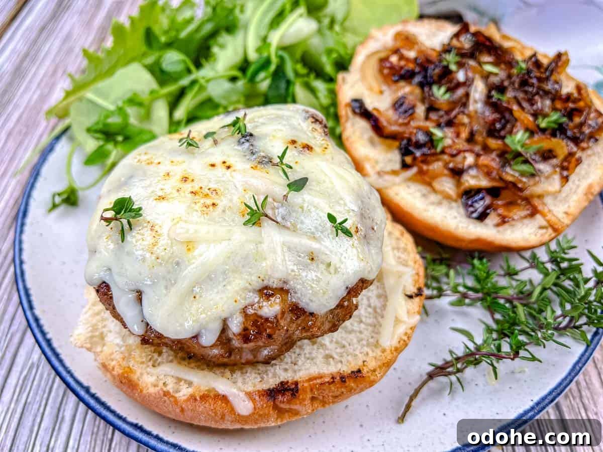 31 Memorial Day Recipes to Start Cookout Season Right 16 Close-up shot of Grilled French Onion Pork Burgers on a Ninja Woodfire Outdoor Grill topped with cheesy onion on a plate.