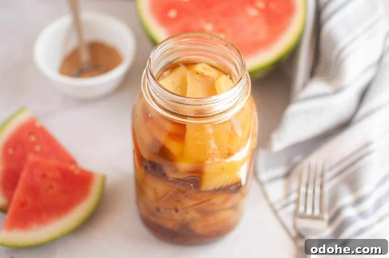 31 Memorial Day Recipes to Start Cookout Season Right 19 A jar of pickled watermelon rind sits on a white surface, with watermelon slices, a striped cloth, a fork, and a small bowl of spices in the background.