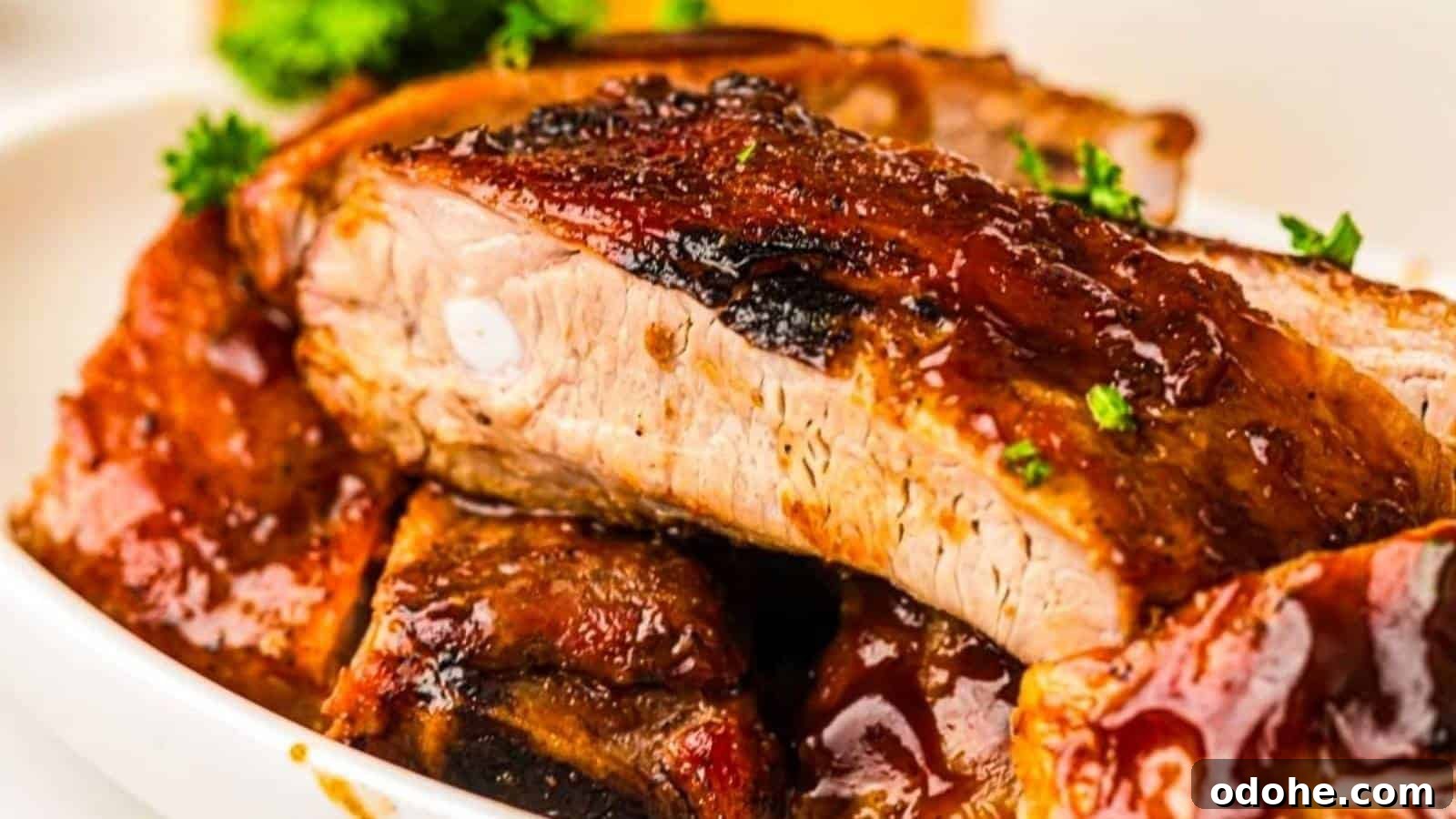 31 Memorial Day Recipes to Start Cookout Season Right 3 Close-up of Grilled ribs covered in sauce, garnished with chopped parsley, served on a white plate.