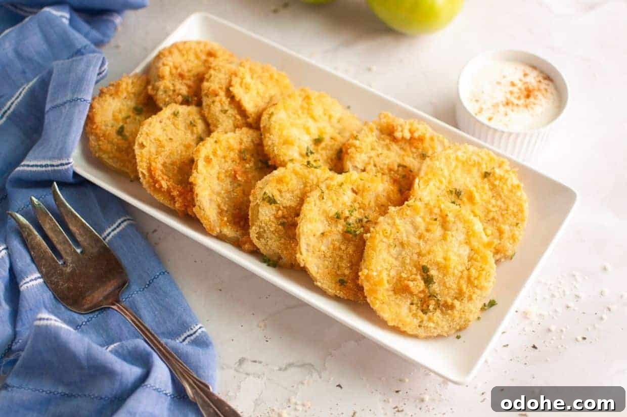 31 Memorial Day Recipes to Start Cookout Season Right 21 A rectangular white plate with fried green tomato slices garnished with herbs, a small cup of dipping sauce, a fork, and a blue napkin on the side.