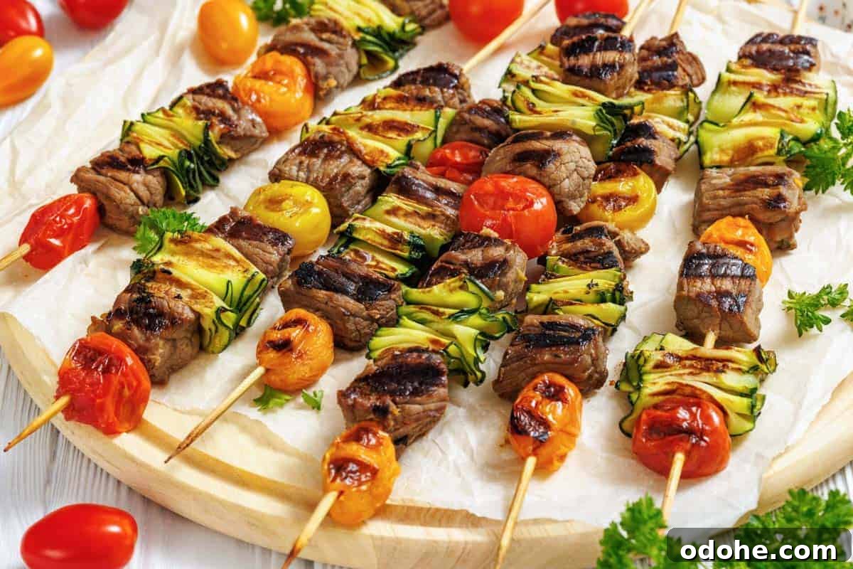 31 Memorial Day Recipes to Start Cookout Season Right 22 A wooden round serving board is covered with white parchment paper, displaying numerous grilled steak and veggie skewers arranged horizontally across it.