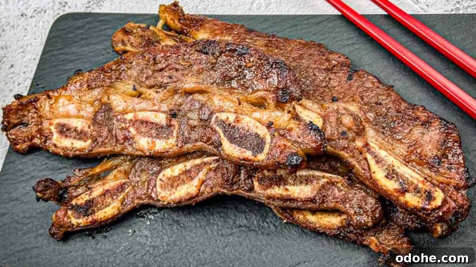 31 Memorial Day Recipes to Start Cookout Season Right 25 Korean Galbi Ribs on a slate platter with red chopsticks beside them.